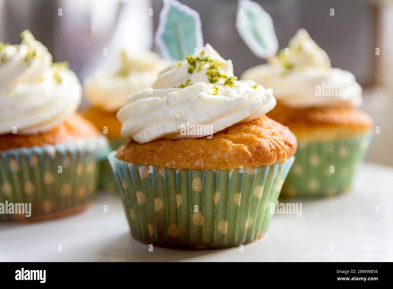 Tasse Kuchen mit Limettenglasur und Limettenschale auf dem Sahnehäubchen und Kuchenfahnen Stockfoto