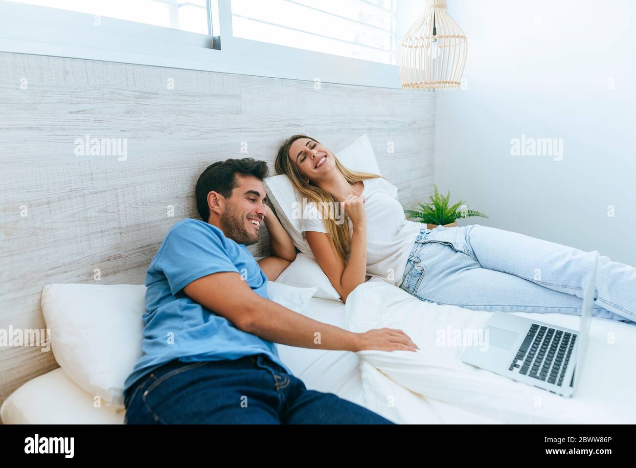 Glückliches Paar, das sich einen Film auf dem Laptop ansieht, während es zu Hause auf dem Bett liegt Stockfoto