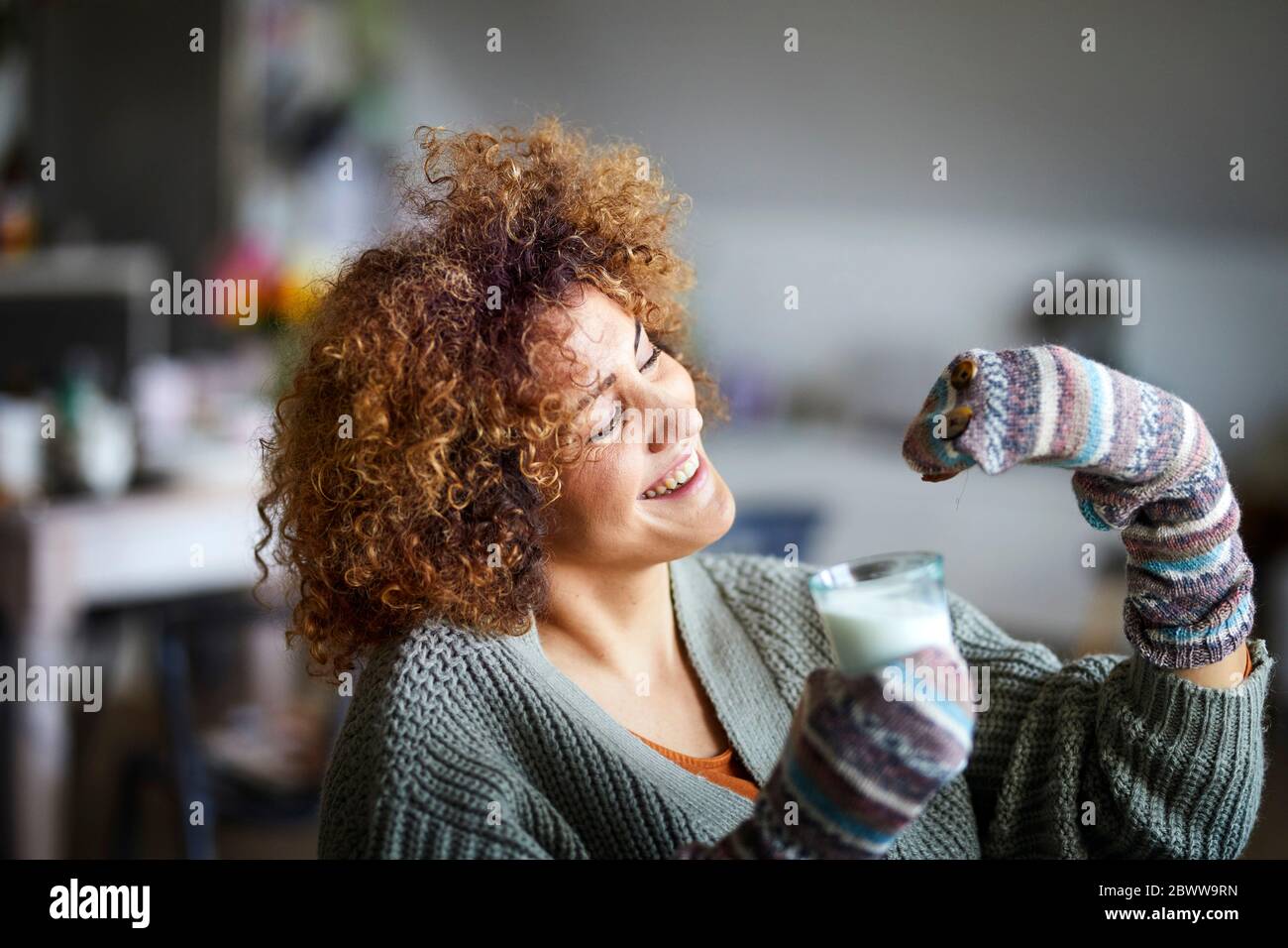 Glückliche Frau spielt mit der Handpuppe, hält ein Glas Milch Stockfoto