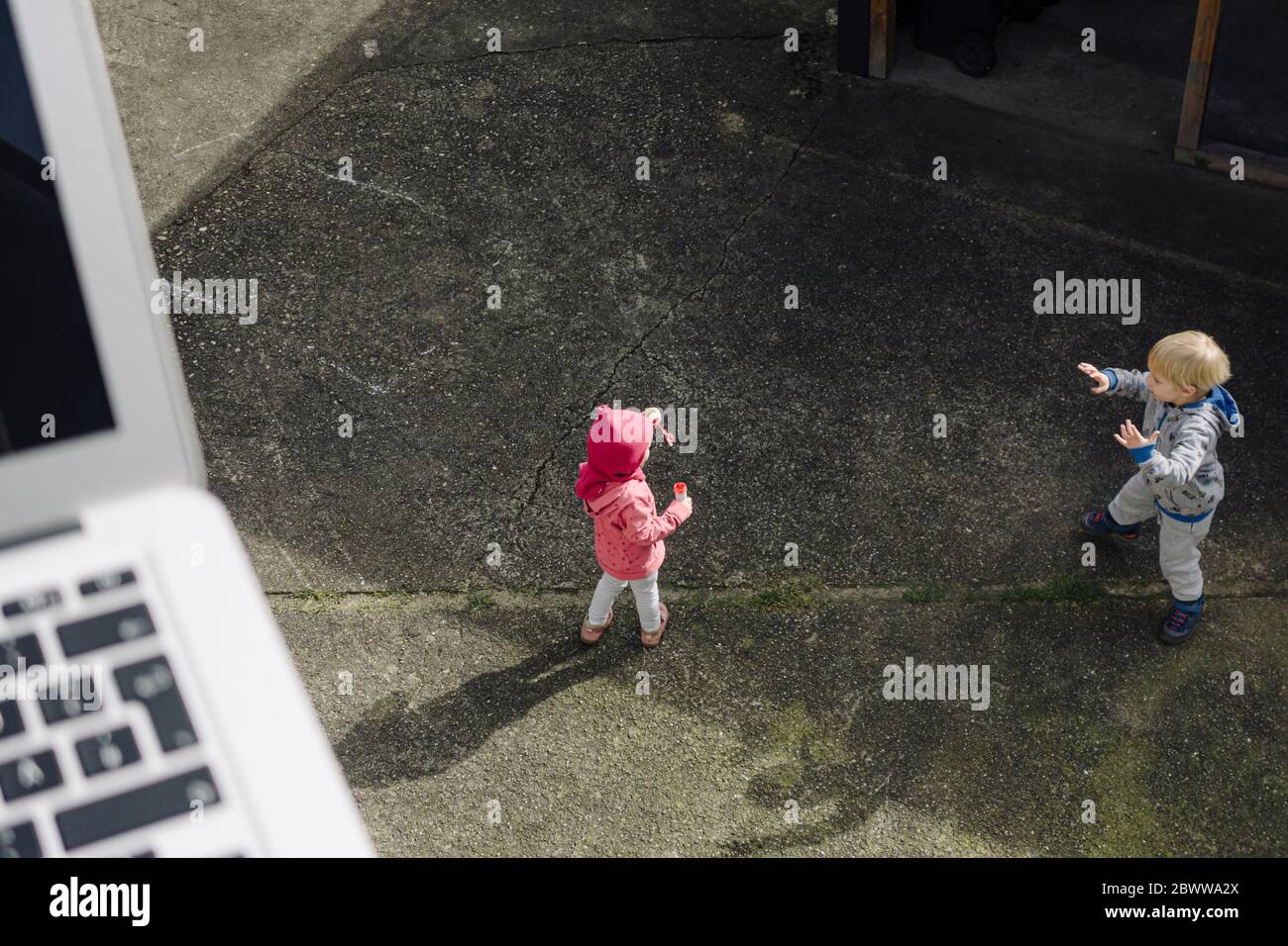 Geschwister spielen zusammen auf Hof mit Laptop im Vordergrund Stockfoto