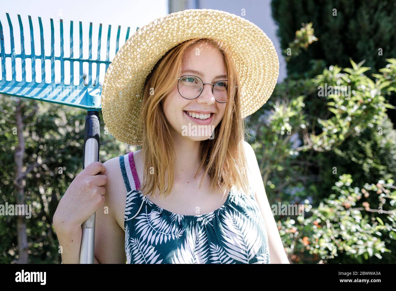 Porträt der lächelnde junge Frau mit Rechen im Garten Stockfoto