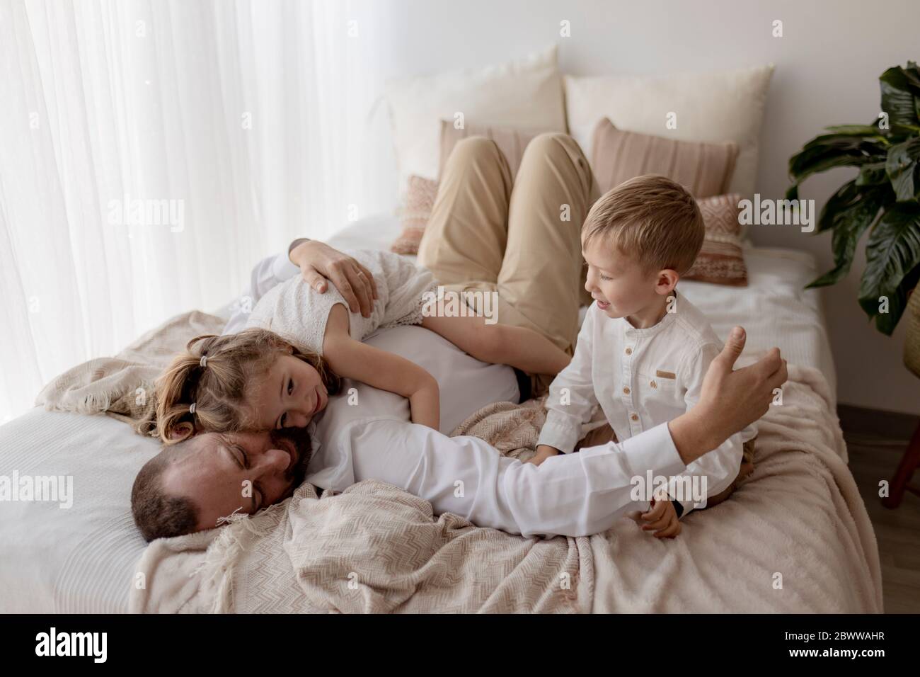Vater liegt auf dem Bett und kuschelt mit seinen beiden Kindern Stockfoto