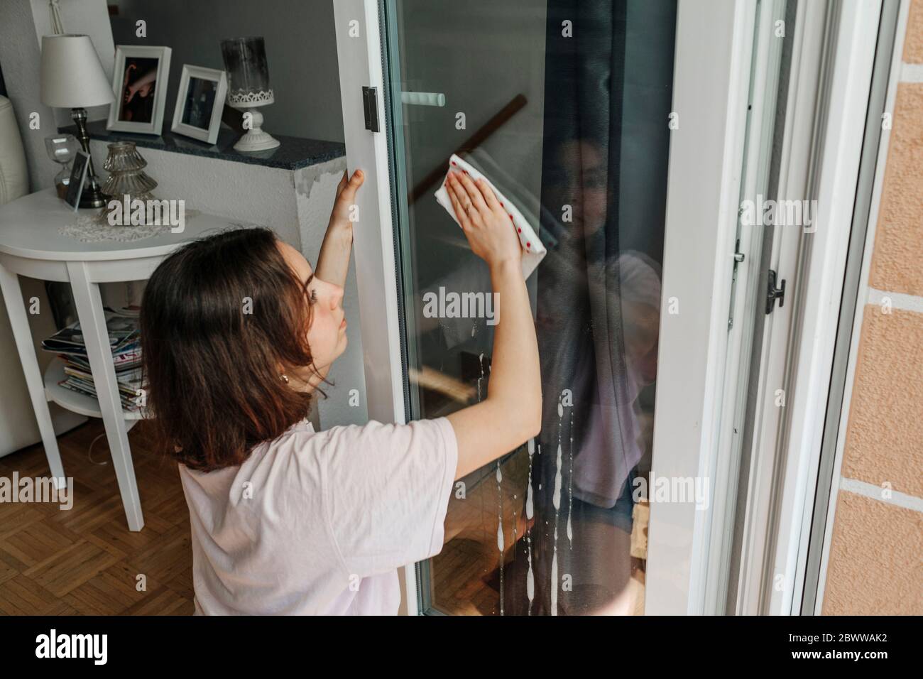 Teenager Mädchen putzt Glasscheibe der Balkontür Stockfoto