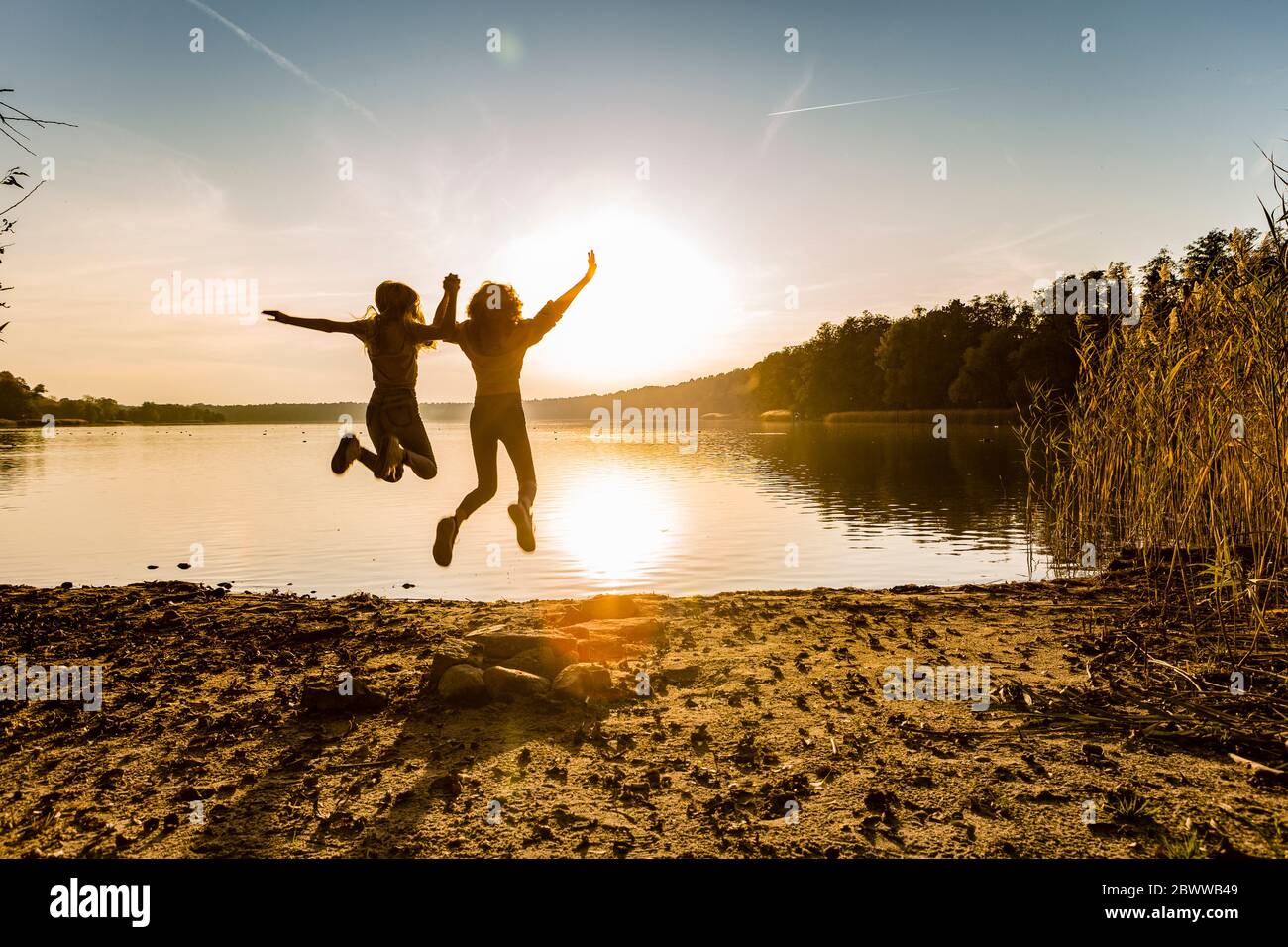 Freunde springen in der Luft am Seeufer gegen den Himmel während des Sonnenuntergangs Stockfoto