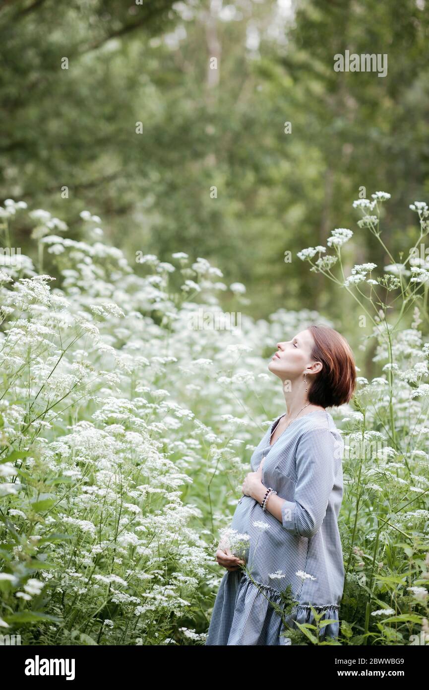 Schwangere Frau mit Händen auf dem Bauch entspannen inmitten von Blumen im Park Stockfoto