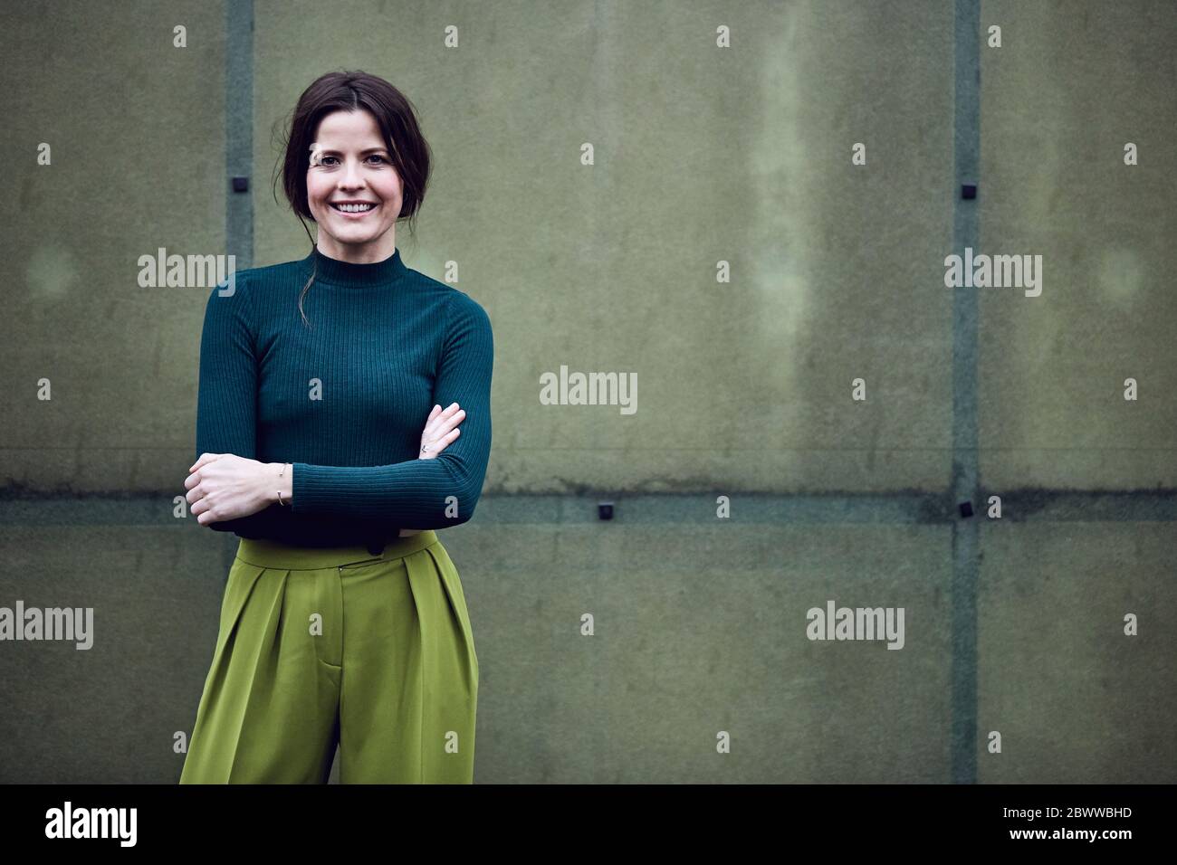 Porträt einer lächelnden Geschäftsfrau, die an einer grünen Wand steht Stockfoto