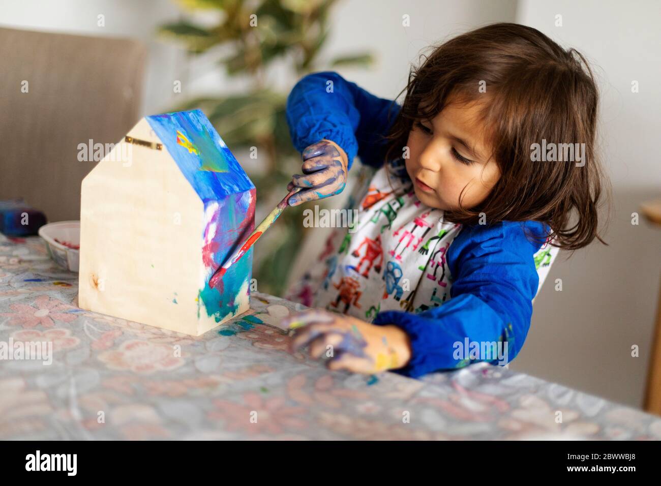 Nettes Mädchen Malerei kleine hölzerne Modell Haus mit Pinsel im Wohnzimmer Stockfoto