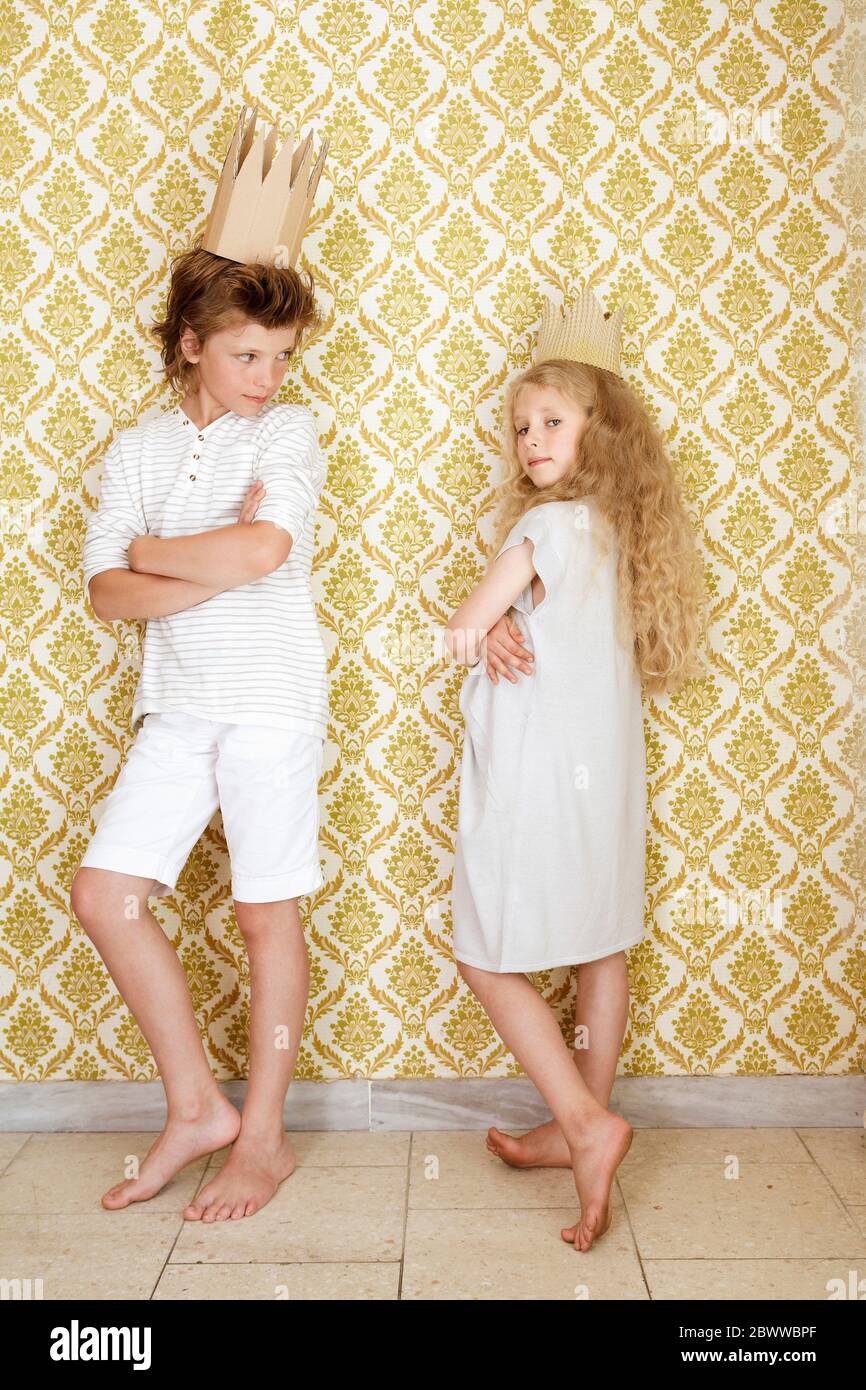 Junge und Mädchen stehen an einer Wand und tragen Pappkronen Stockfoto