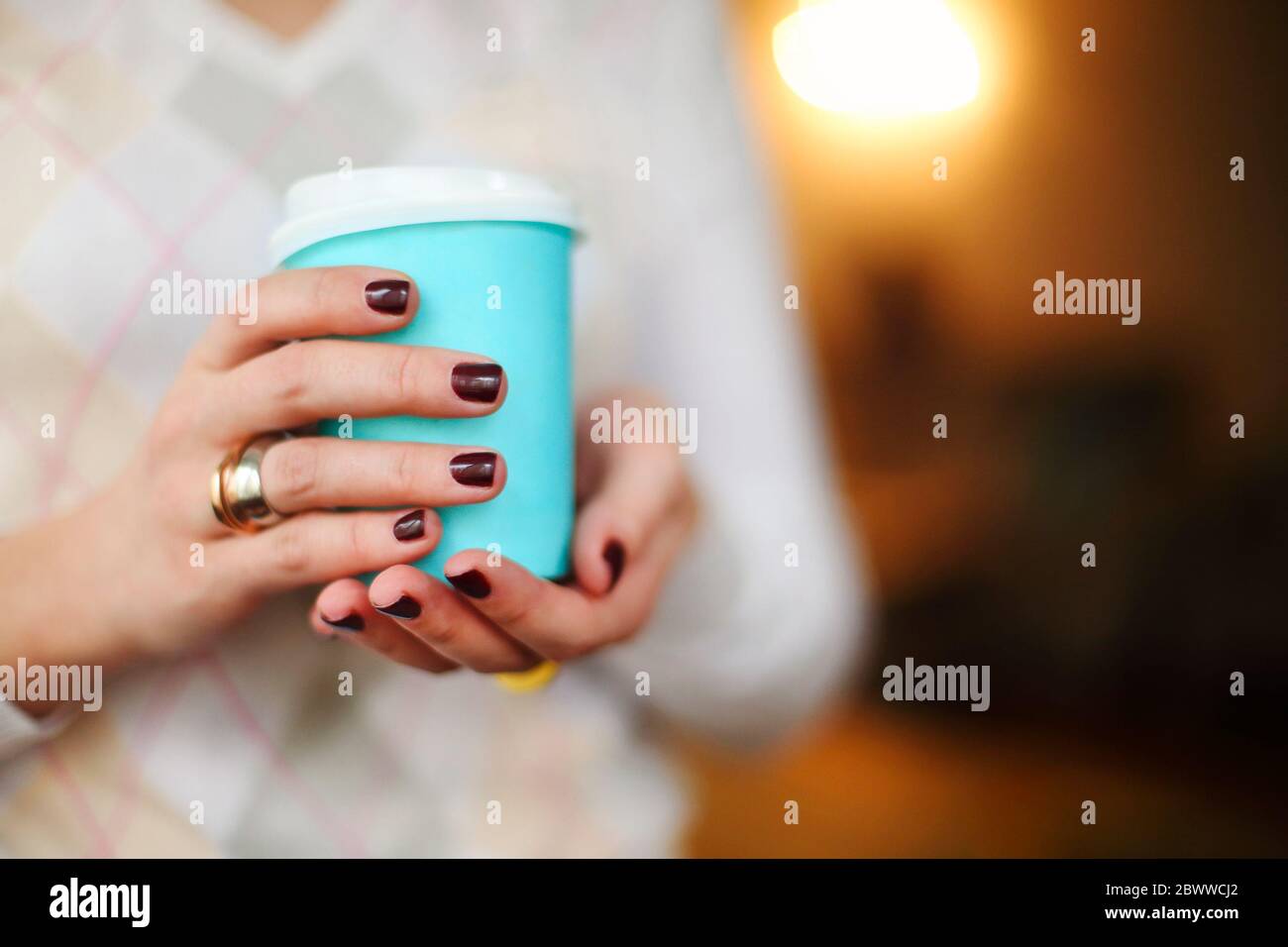 Ernte anonyme Frau in warmen Pullover mit dunkler Maniküre hält Einweg Tasse Kaffee während der Ruhepause am Holztisch Stockfoto
