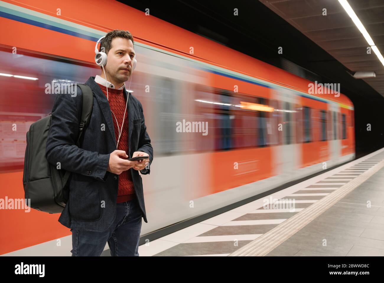 Geschäftsmann hört Musik über das Handy, während er auf dem Bahnsteig gegen die U-Bahn steht Stockfoto