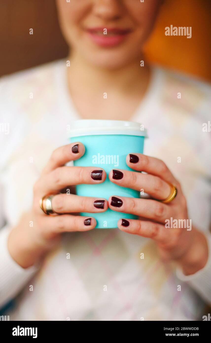 Ernte anonyme Frau in warmen Pullover mit dunkler Maniküre hält Einweg Tasse Kaffee während der Ruhepause am Holztisch Stockfoto