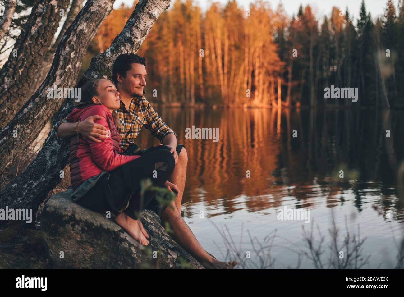 Junges Paar sitzt auf Stein am Seeufer, Blick auf den Sonnenuntergang Stockfoto