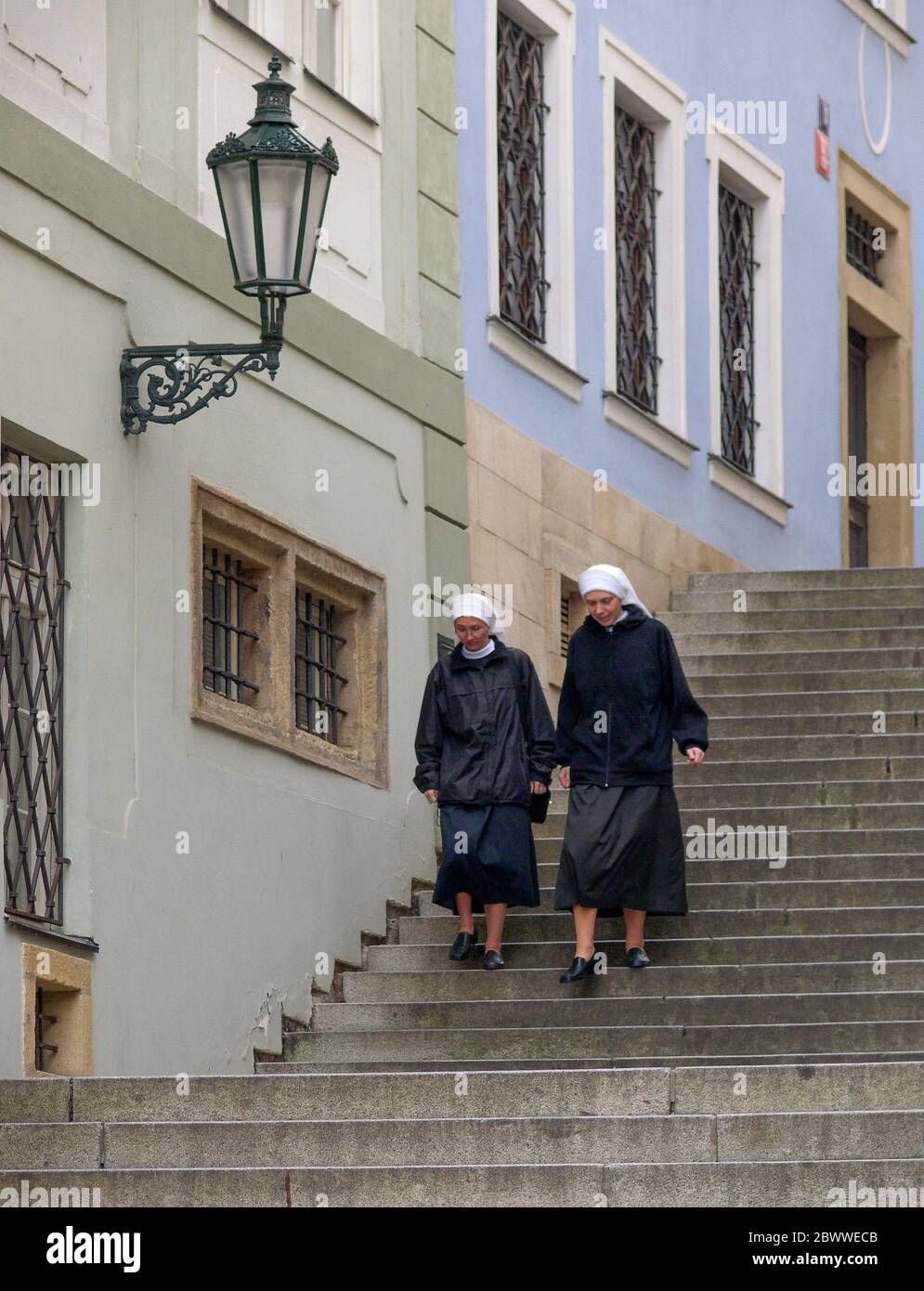 Nonnen gehen steile Stufen an der Prager Burg - Pražský Hrad mit der Skyline der Stadt hinunter. Die Burg ist das offizielle Büro des Präsidenten der Tschechischen Republik Stockfoto