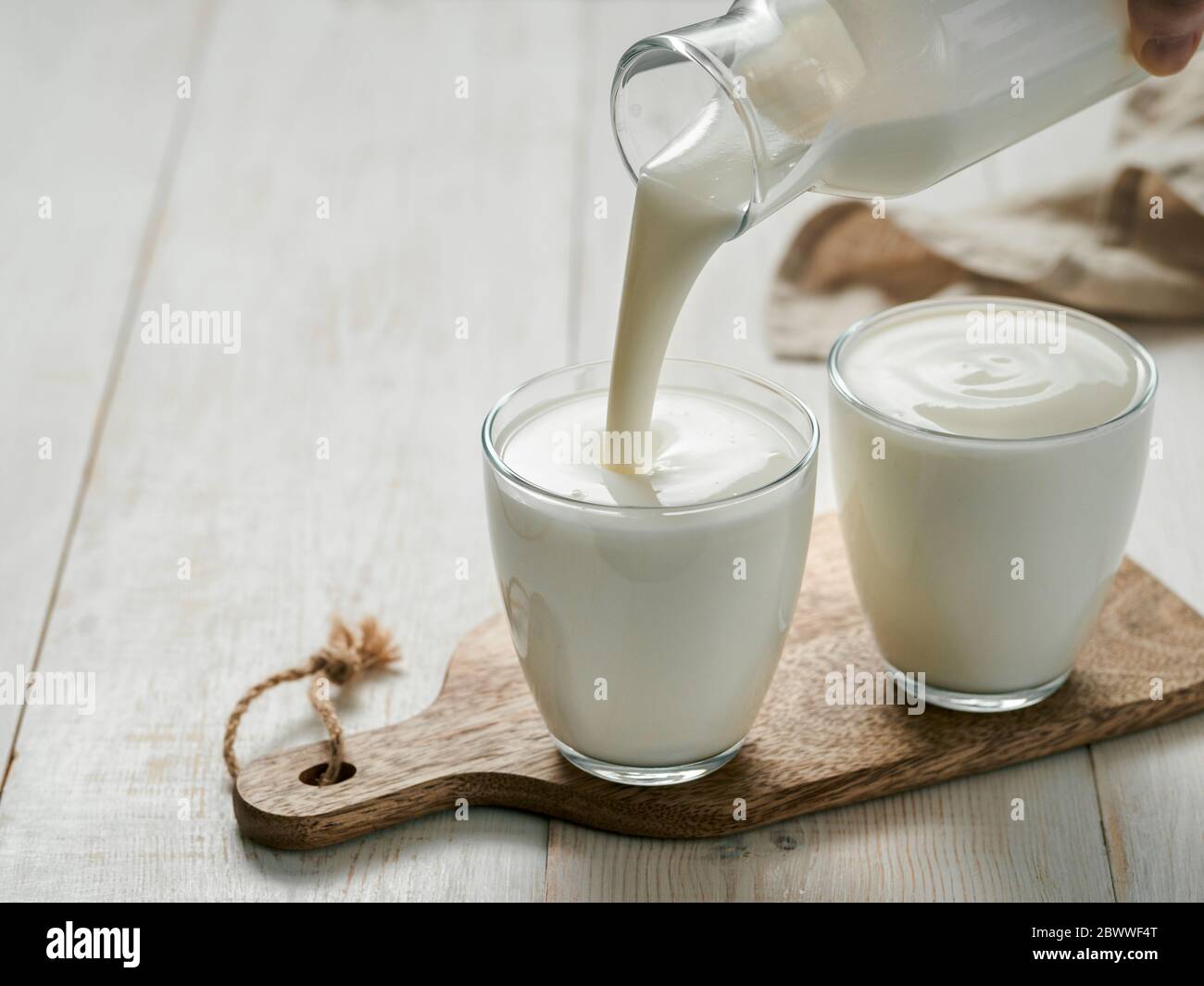 Hausgemachte Kefir, Buttermilch oder Joghurt mit Probiotika gießen. Joghurt aus Glasflasche auf weißem Holzhintergrund. Probiotische kalt fermentierte Milchgetränk. Trendige Speisen und Getränke. Kopierbereich links Stockfoto