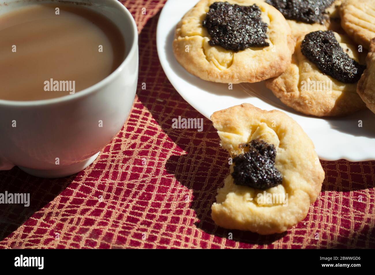 Gebissene Plätzchen mit Mohnfüllung und Kaffee bei Tageslicht, Background, Food-Fotografie Stockfoto
