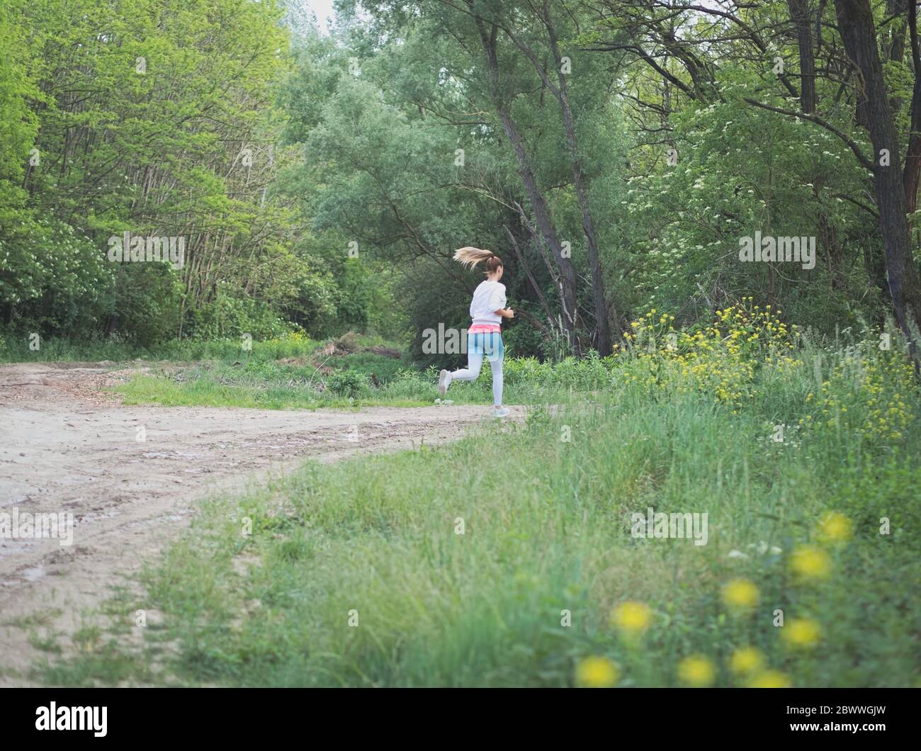 Junge Blonde kaukasische Frau läuft im Wald auf einem Dirt Road Stockfoto