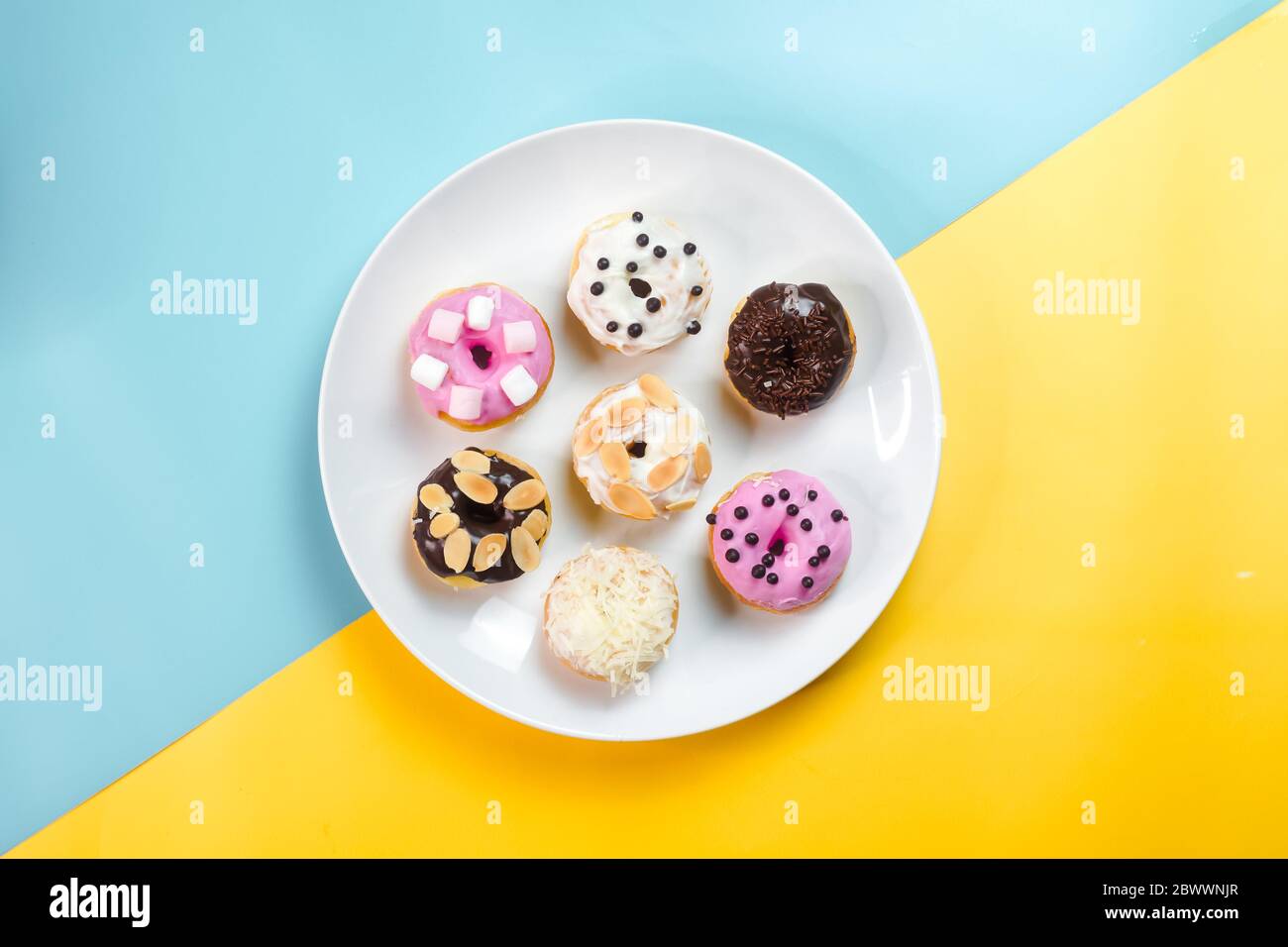 Bunte Donuts auf einem weißen Teller auf kreativem Hintergrund serviert. Stockfoto