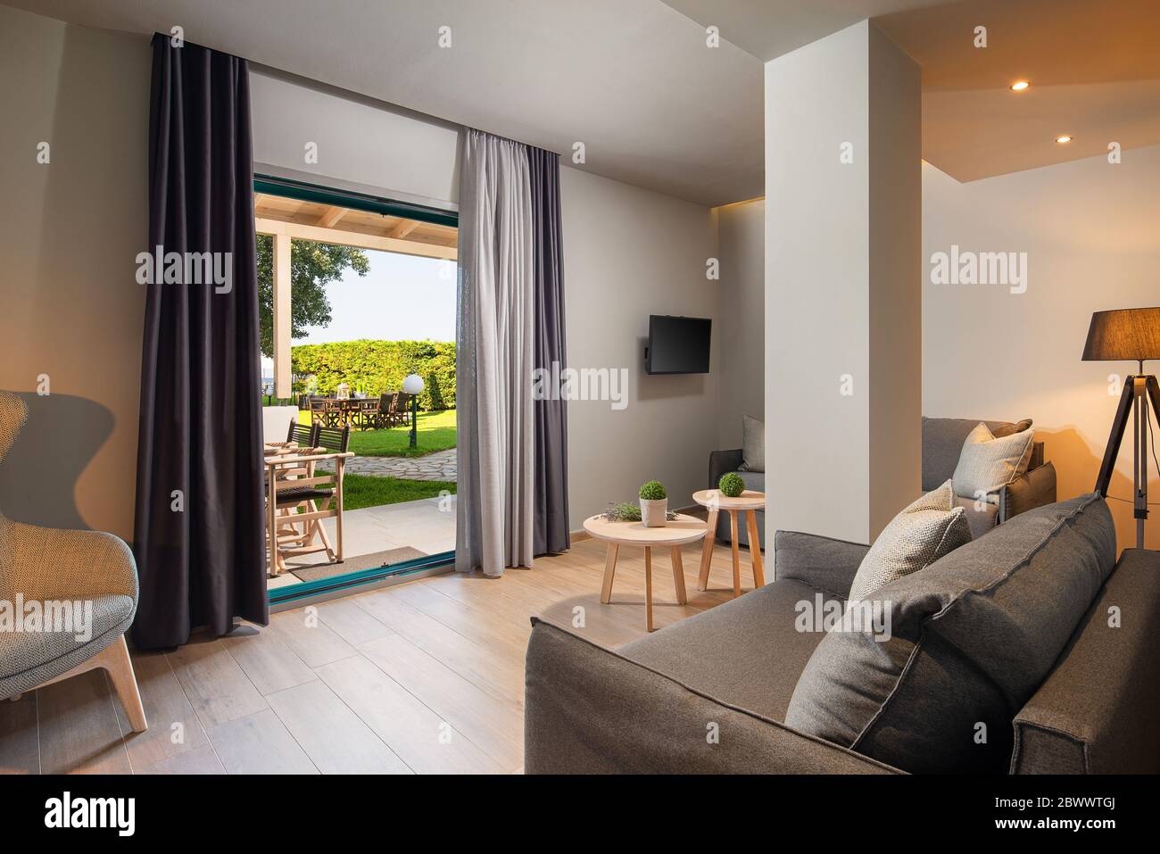 Modernes grau-Holz-Wohnzimmer mit großem französischen Fenster und grüner Gartenterrasse. Umweltfreundliches Innenkonzept Stockfoto