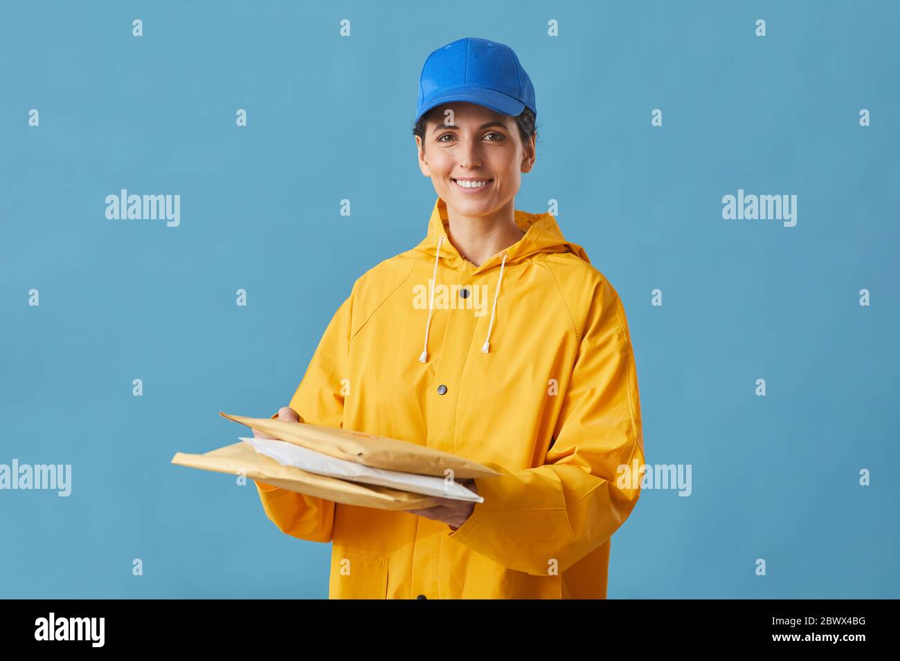 Porträt einer jungen Frau in Uniform, die Pakete in den Händen hält und die Kamera isoliert auf blauem Hintergrund lächelt Stockfoto