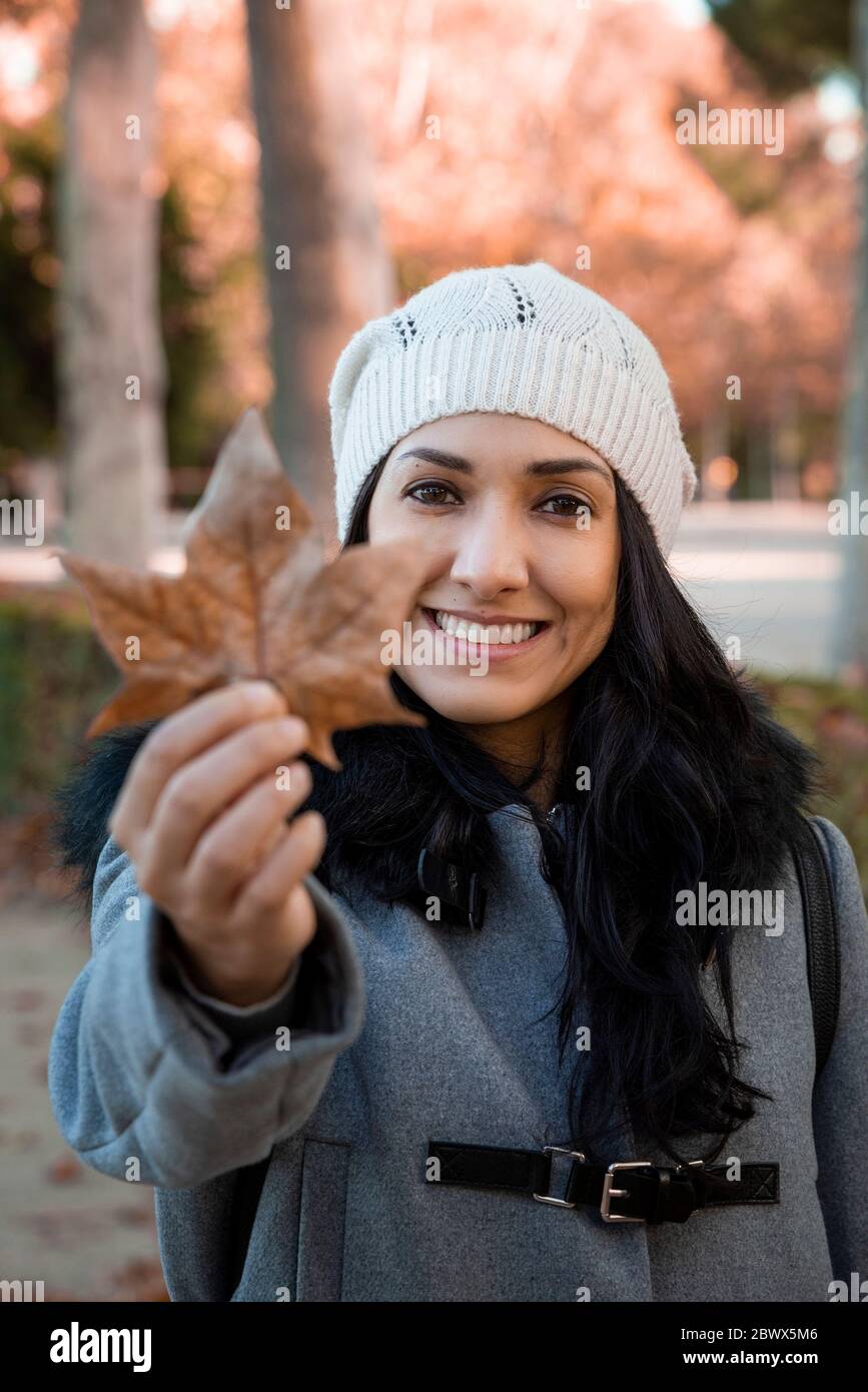 Porträt einer jungen lateinischen Frau lächelnd. Sie hält das typische Herbstlaubblatt. Stockfoto