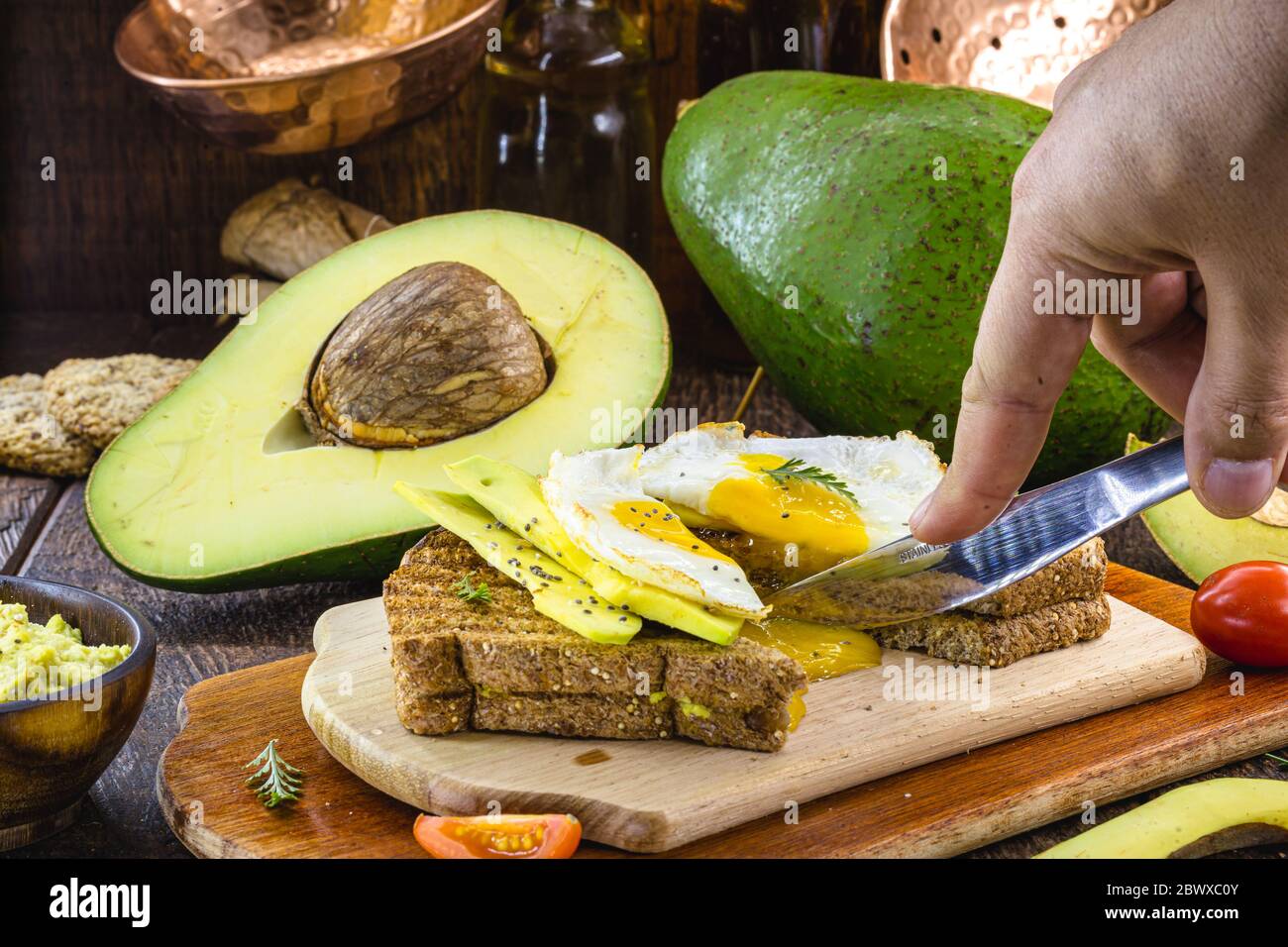 Handschneidende Avocado-Toast mit gebratenem Ei in der Mitte, Eigelb tropft. Gesundes Frühstück. Stockfoto