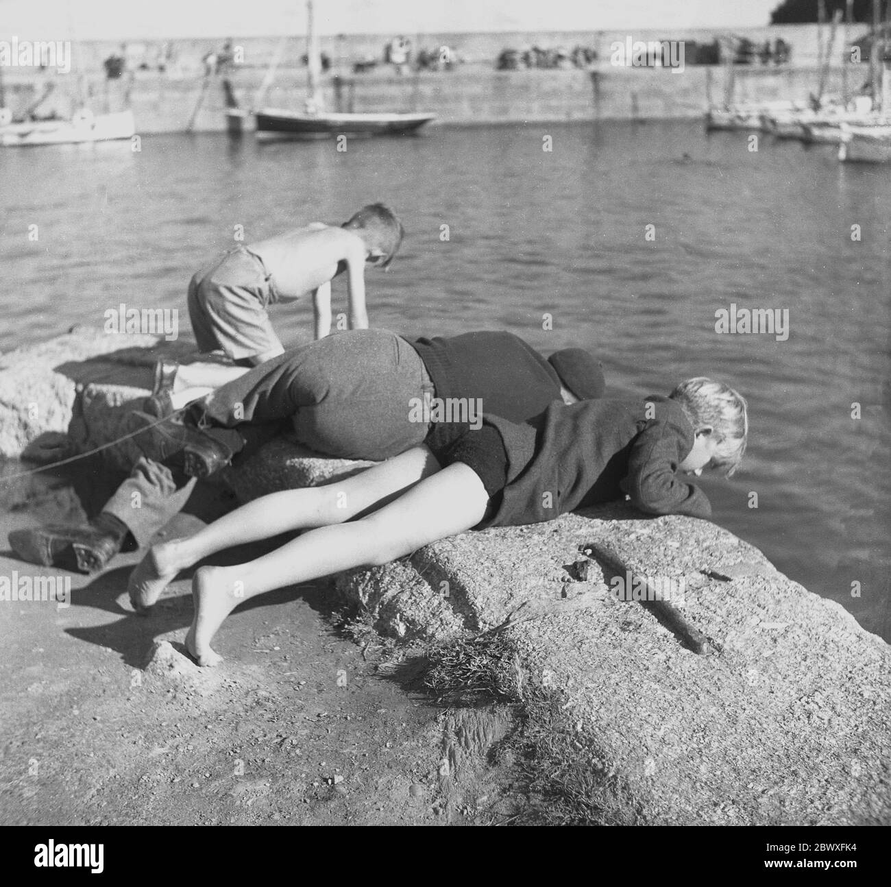 1950er Jahre, historisch, auf der Suche nach Fisch, ein Mann in einer Baskenmütze, möglicherweise ein lokaler Fischer und zwei junge Jungen an einem Hafen lehnen sich über den Rand in das Wasser unten zu schauen, um zu sehen, ob es irgendwelche Fische mit ihren Netzen zu fangen, England, Großbritannien. Stockfoto