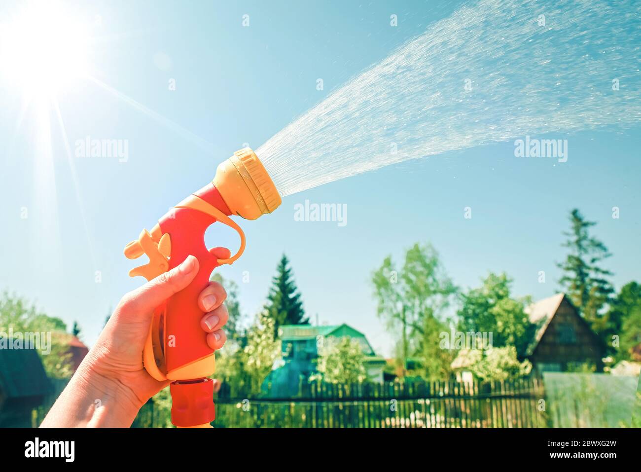 Hand hält gelben Schlauch mit Düse auf Hintergrund des blauen Himmels mit Wasserspritzern Stockfoto