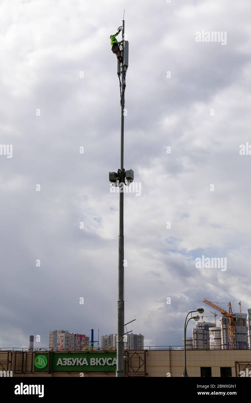 Moskau/Russland - Mai 2020: Silhouette eines Mannes auf einem Mast mit Telekommunikationsgeräten, der eine Antenne gegen einen bewölkten Himmel repariert Stockfoto