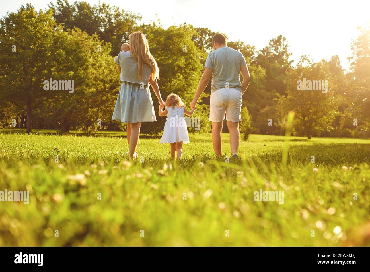 Fröhliche Familienspaziergänge auf dem Gras im Sommerpark. Mutter Vater und Kinder, die in der Natur spielen. Kinderschutztag. Stockfoto