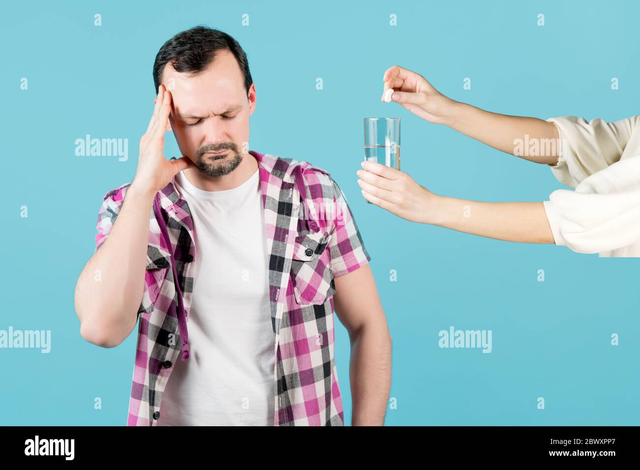 Der Mann hat Kopfschmerzen und das Mädchen bietet ihm eine an Lösliche Pille und ein Glas Wasser Stockfoto