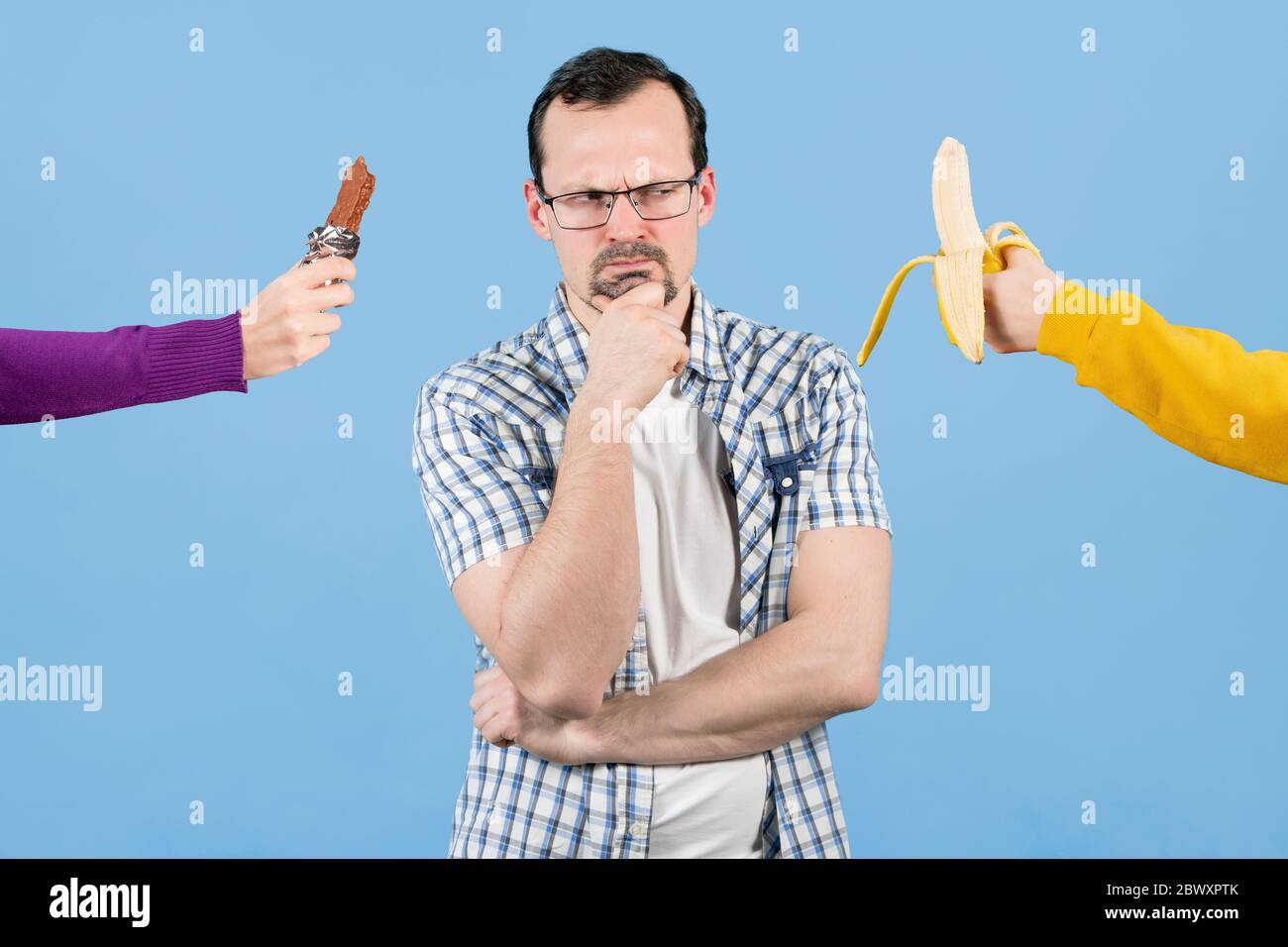 Ein Mann steht vor der Wahl zwischen etwas zu essen - eine Banane oder eine Schokoladenriegel. Schlechte und gesunde Snacks Stockfoto