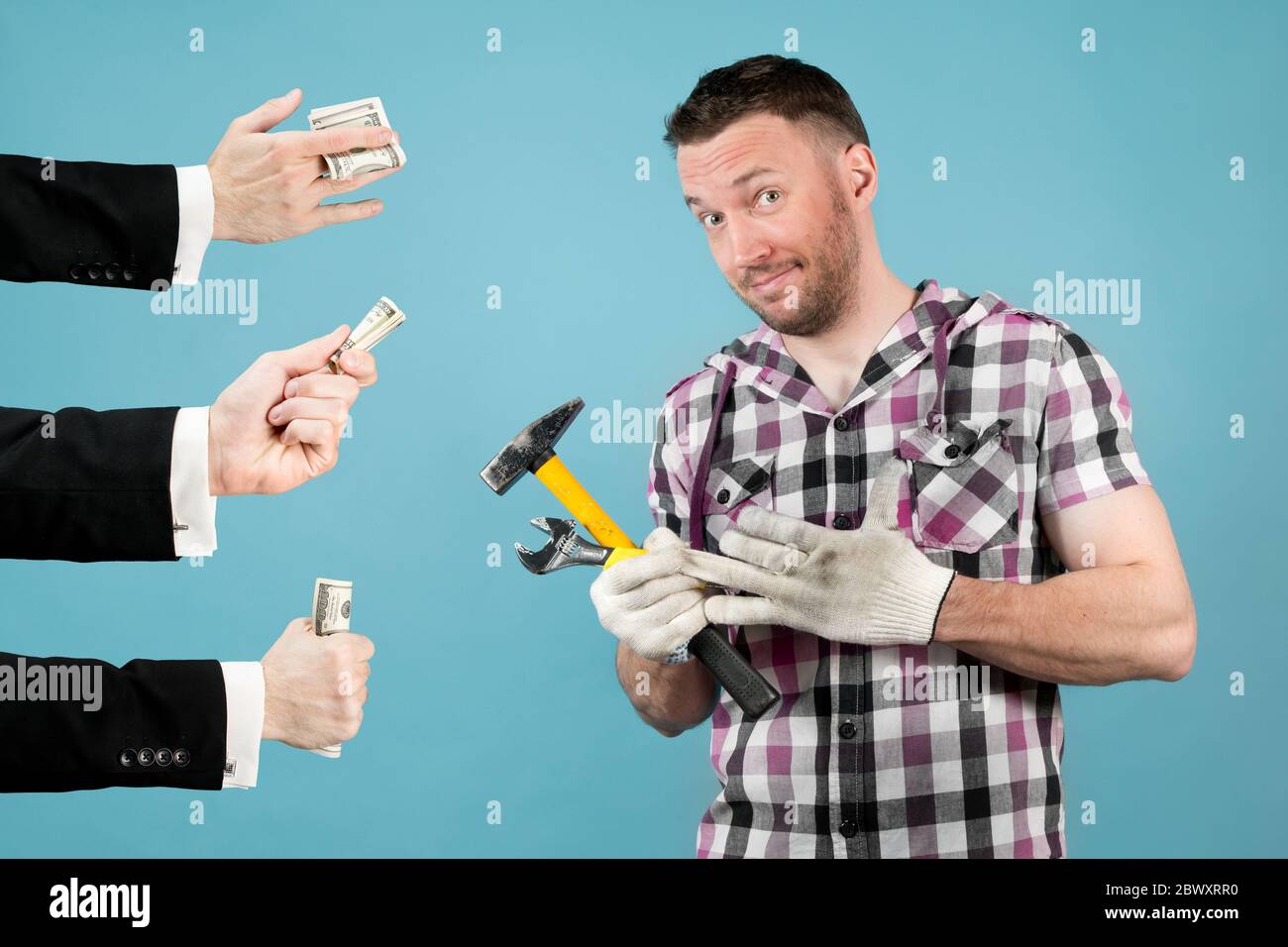 Ein harter Arbeiter mit Werkzeugen in den Händen zieht ihm einen Schutzhandschuh aus der Hand und lächelt, weil ihm die Hände schöner Männer Geld reichen. High Stockfoto