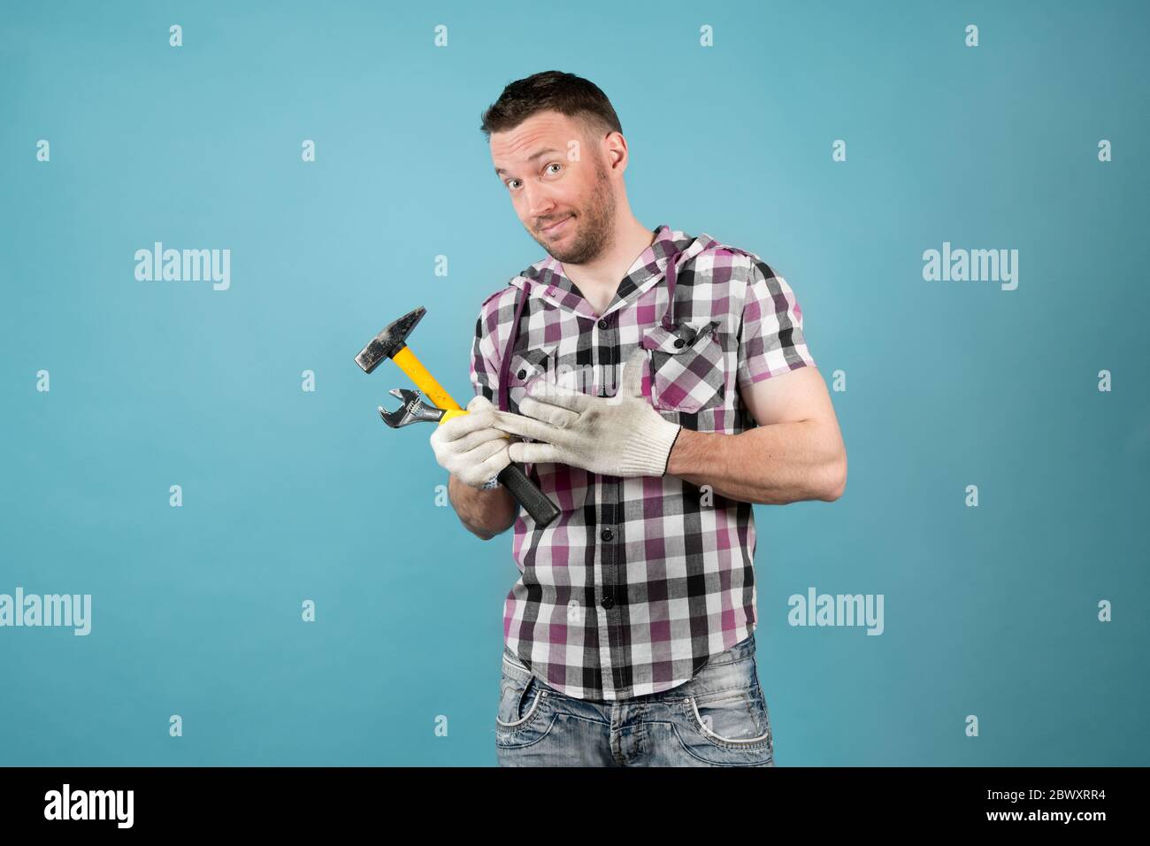 Schmutziger harter Arbeiter in einem schlauen Hemd mit Werkzeugen in den Händen zieht einen Schutzhandschuh aus seiner Hand und lächelt schlaff Stockfoto