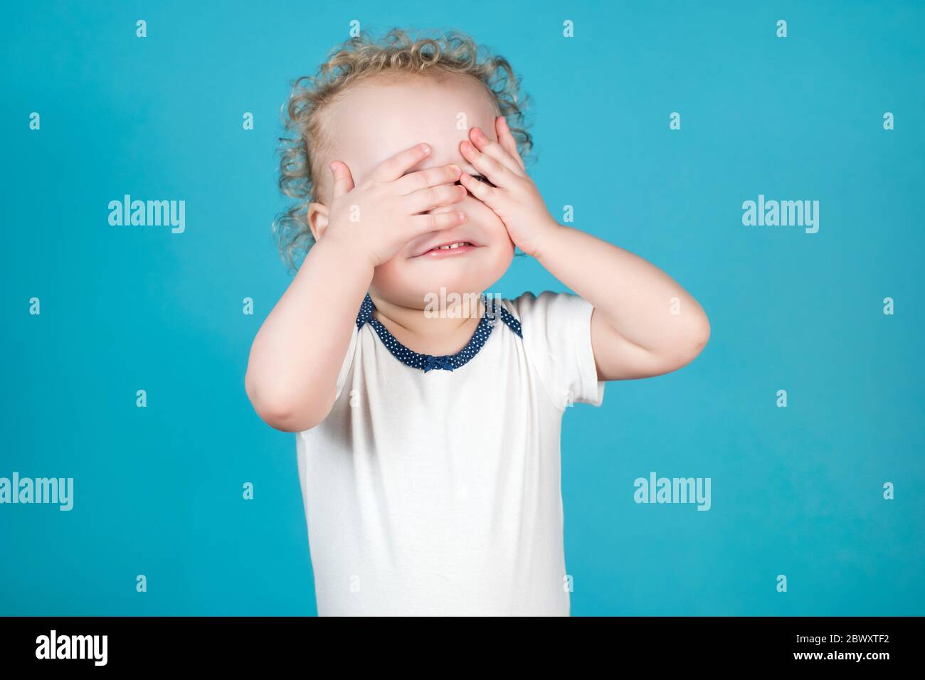 Zwei Jahre alt lockig Baby Mädchen bedeckt ihr Gesicht mit Lächelnde Hände Stockfoto