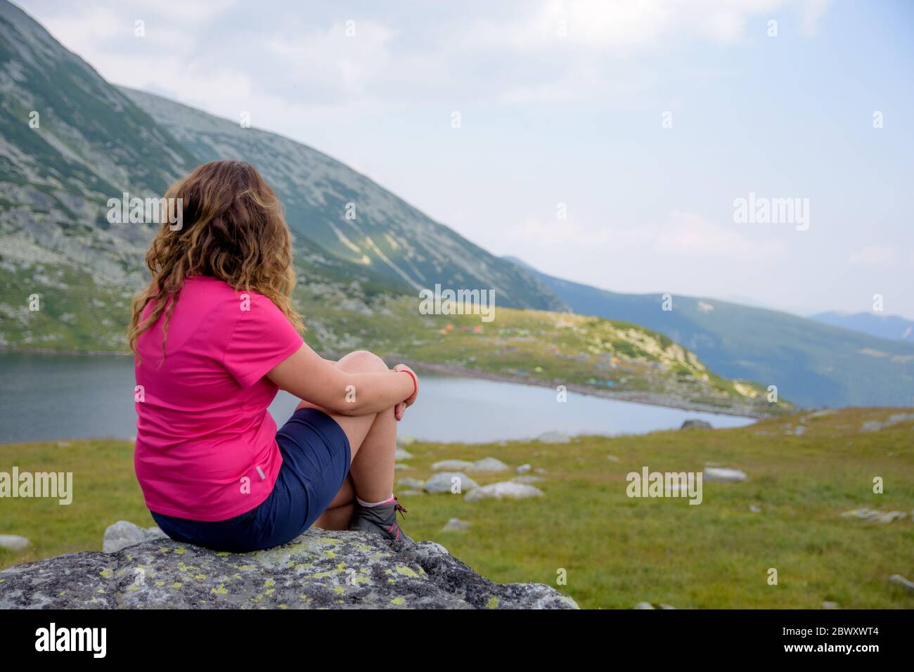 Junges Mädchen mit farbigen Hemd und welligen Haaren Blick über Gletschersee in Karpaten Berge in Rumänien Stockfoto