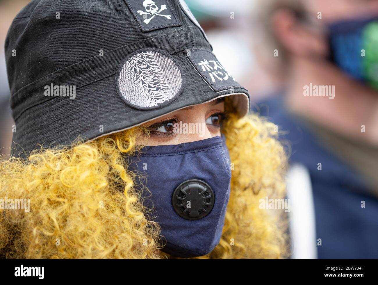 Porträt einer jungen Frau mit lockigen gelben Haaren, die eine Gesichtsmaske und einen Hut auf dem protestmarsch von Black Lives Matter UK trägt. London, England, Großbritannien Stockfoto