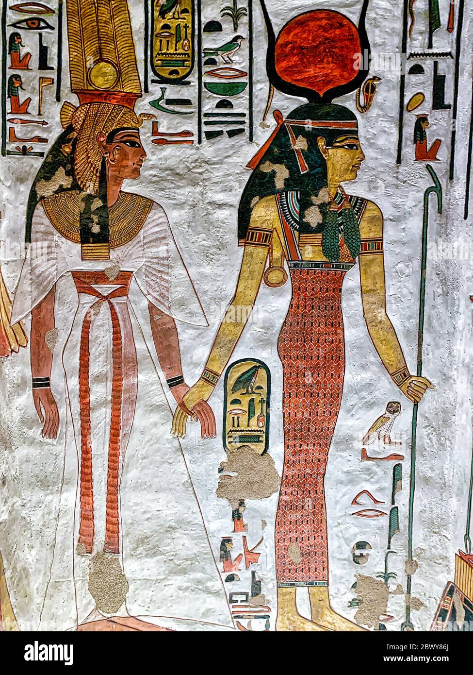 Nefertari, geführt von Isis, trägt ein halbtransparentes weißes Kleid, das mit einer roten Schärpe gebunden ist. ISIS trägt die Sonnenscheibe auf ihrem Kopf zwischen gebogenen Stierkambeln Stockfoto