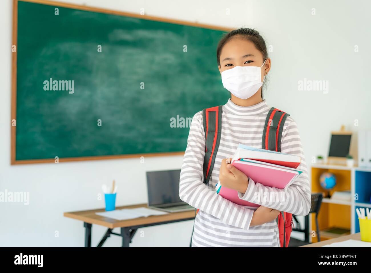 Asiatische Grundschüler Mädchen mit Rucksack und Bücher tragen Masken, um den Ausbruch von Covid 19 im Klassenzimmer zu verhindern, während wieder in der Schule öffnen ihre s Stockfoto
