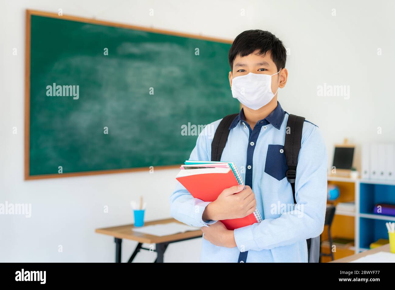 Asiatische Grundschüler Jungen mit Rucksack und Bücher tragen Masken, um den Ausbruch von Covid 19 im Klassenzimmer zu verhindern, während wieder in der Schule öffnen ihre sc Stockfoto