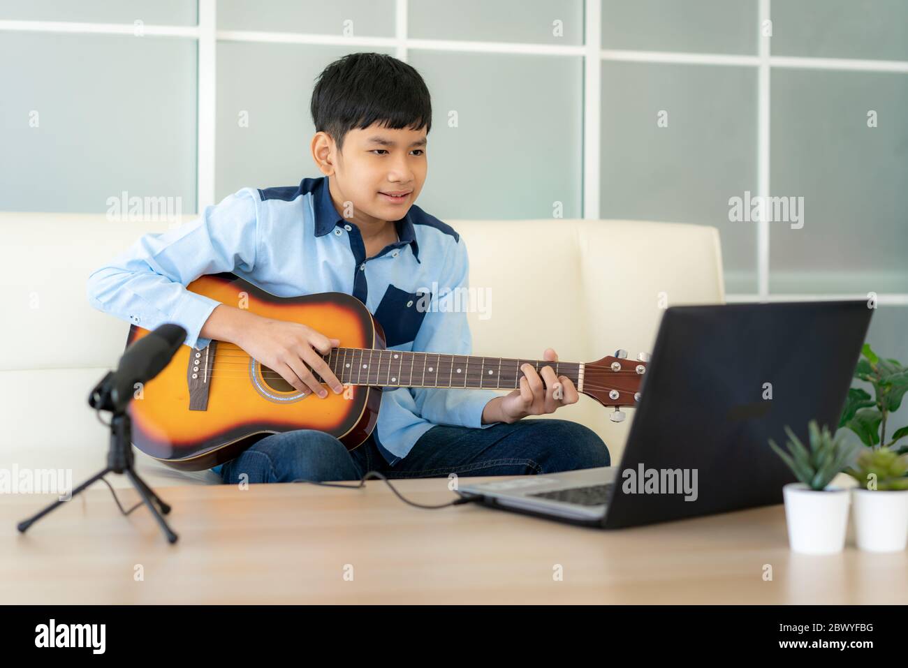Asiatische junge spielen akustische Gitarre und beobachten Online-Kurs auf Laptop beim Üben zu Hause. Asiatische junge virtuelle Happy Hour Treffen für Musik spielen o Stockfoto