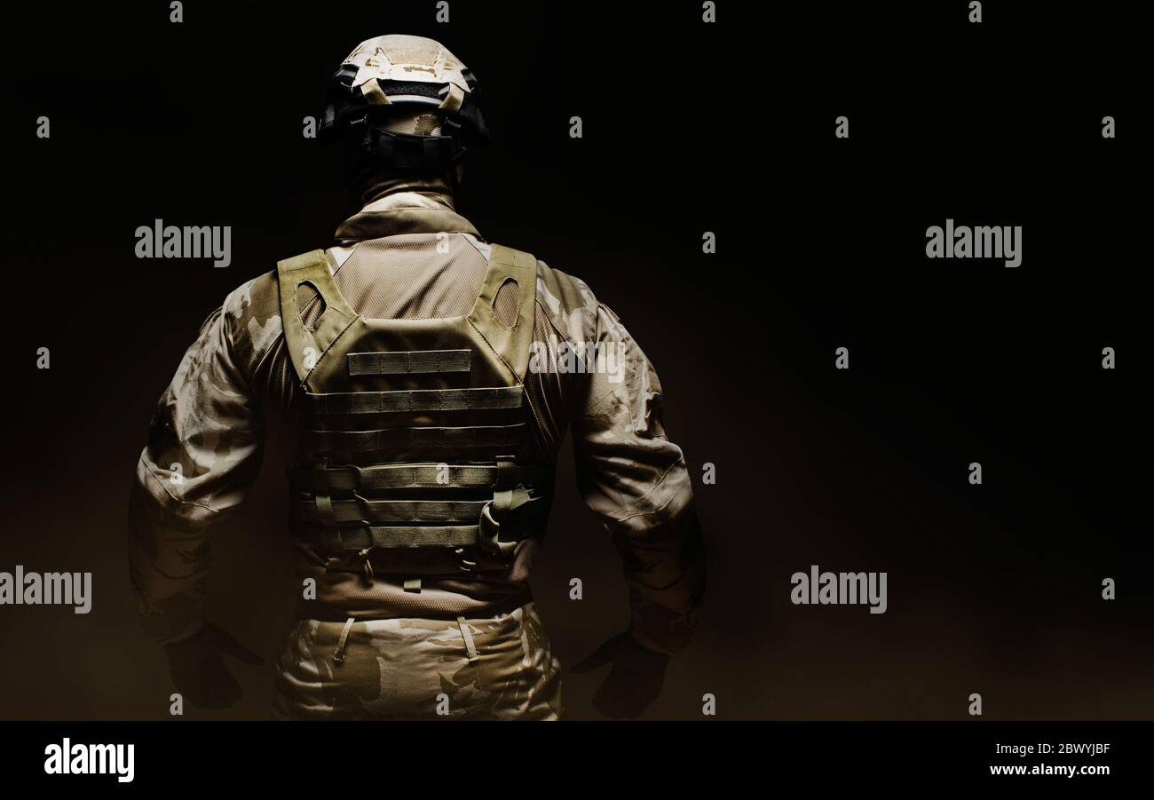 Foto eines voll ausgestatteten Wüste Tarnsoldaten in Maske, Helm, Rüstung und Handschuhe auf schwarzem Hintergrund Rückansicht. Stockfoto