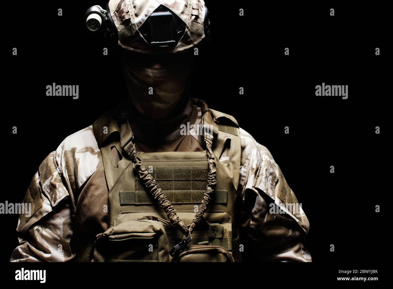 Foto eines voll ausgestatteten Wüste Tarnsoldaten in Maske, Helm, Rüstung und Handschuhe stehen schattig auf schwarzem Hintergrund Vorderansicht. Stockfoto