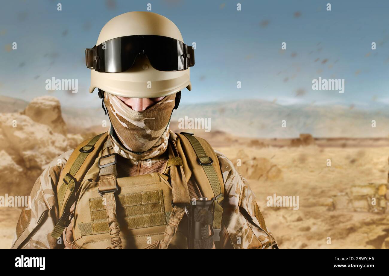 Foto eines voll ausgestatteten Wüstensoldaten in Helm, Rüstung und Brille auf Wüstenhintergrund stehend. Stockfoto