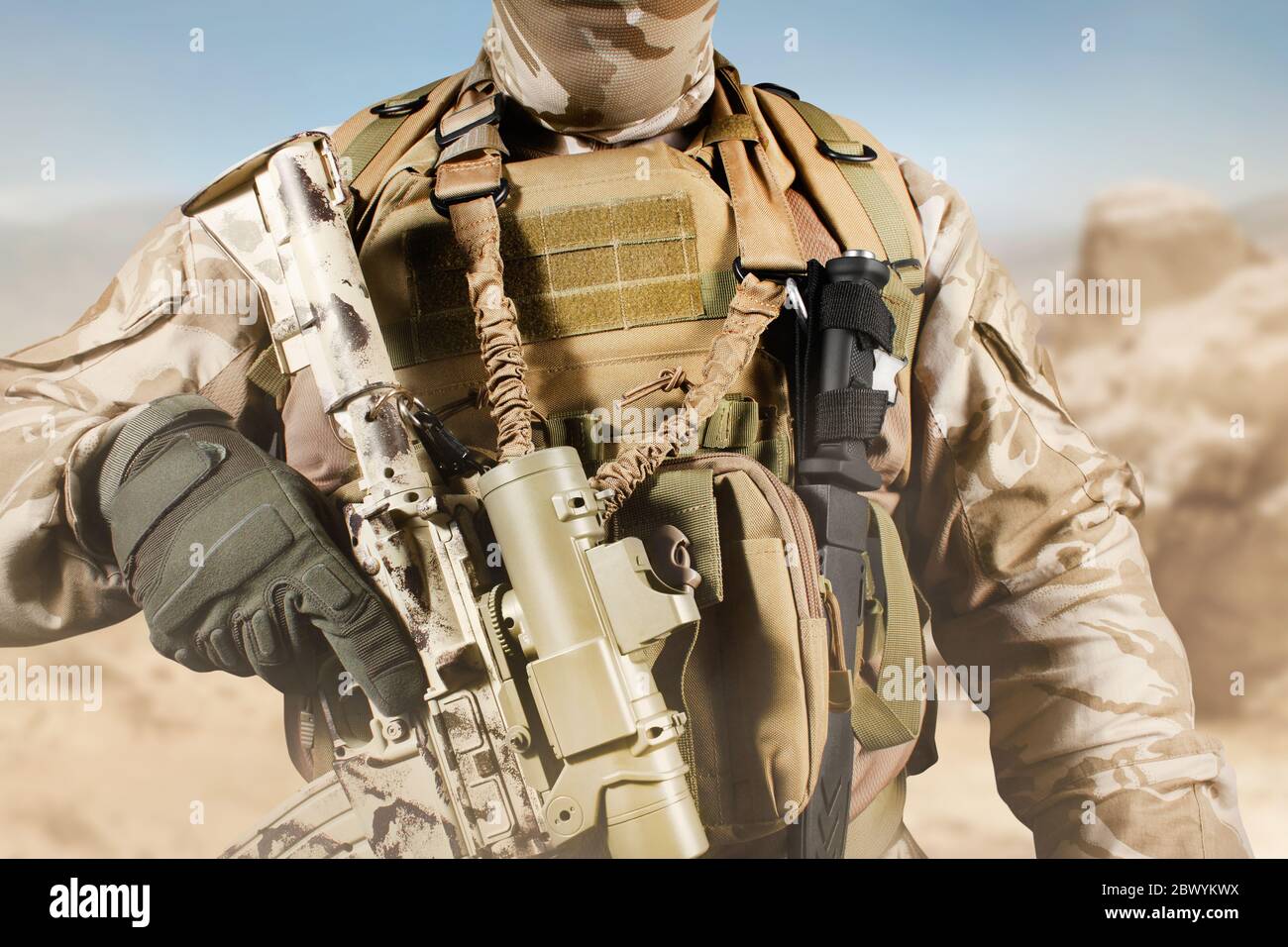 Foto eines voll ausgestatteten Soldaten in Uniform, Rüstung, Helm und Maske mit Gewehr in Wüste Schlachtfeld Hintergrund Nahaufnahme stehen. Stockfoto