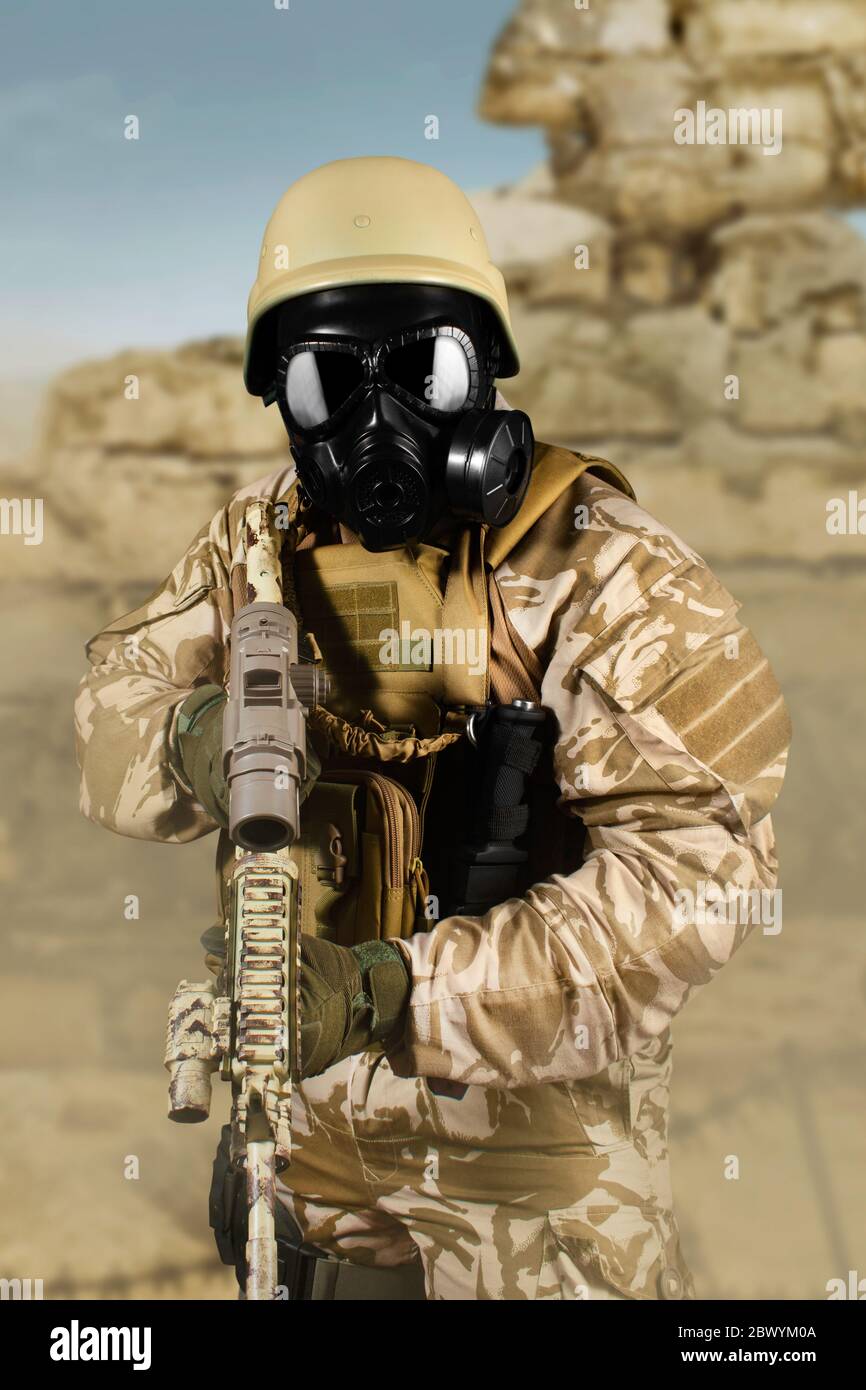 Foto von einem voll ausgestatteten Soldaten in Uniform, Rüstung, Helm und Gasmaske Angriff mit Gewehr in Wüste Schlachtfeld Hintergrund. Stockfoto