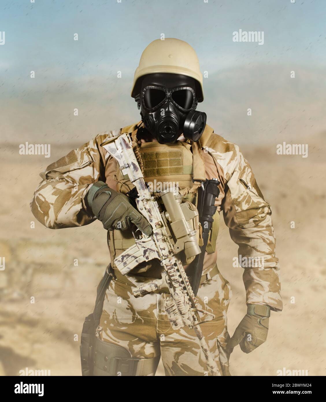 Foto eines voll ausgestatteten Soldaten in Uniform, Rüstung, Helm und Gasmaske mit Gewehr in Wüste Schlachtfeld im Hintergrund Vorderansicht stehen. Stockfoto