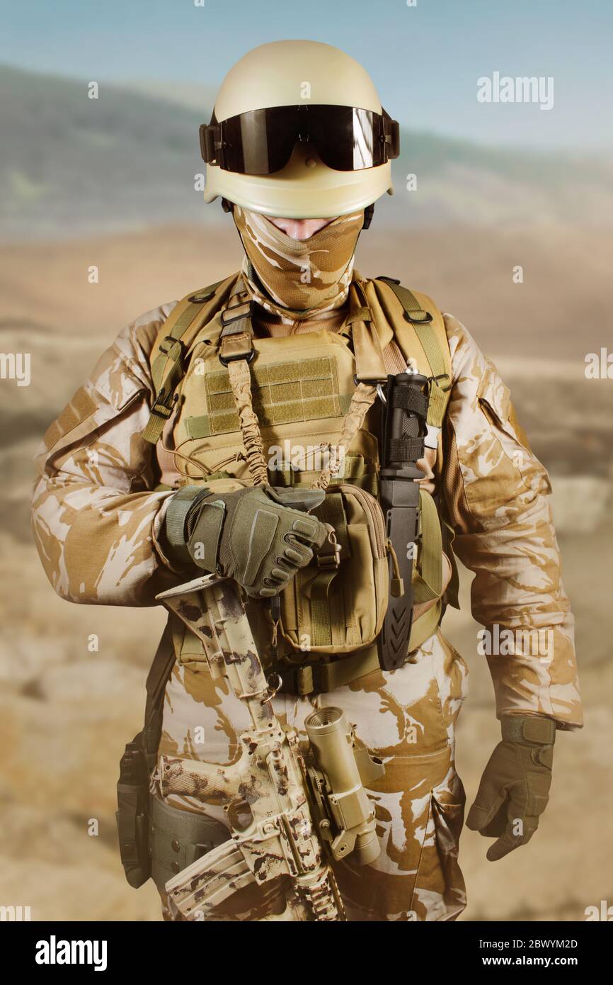 Foto eines voll ausgestatteten Soldaten in Uniform, Rüstung, Helm und Brille in der Wüste stehend und Weste halten. Stockfoto