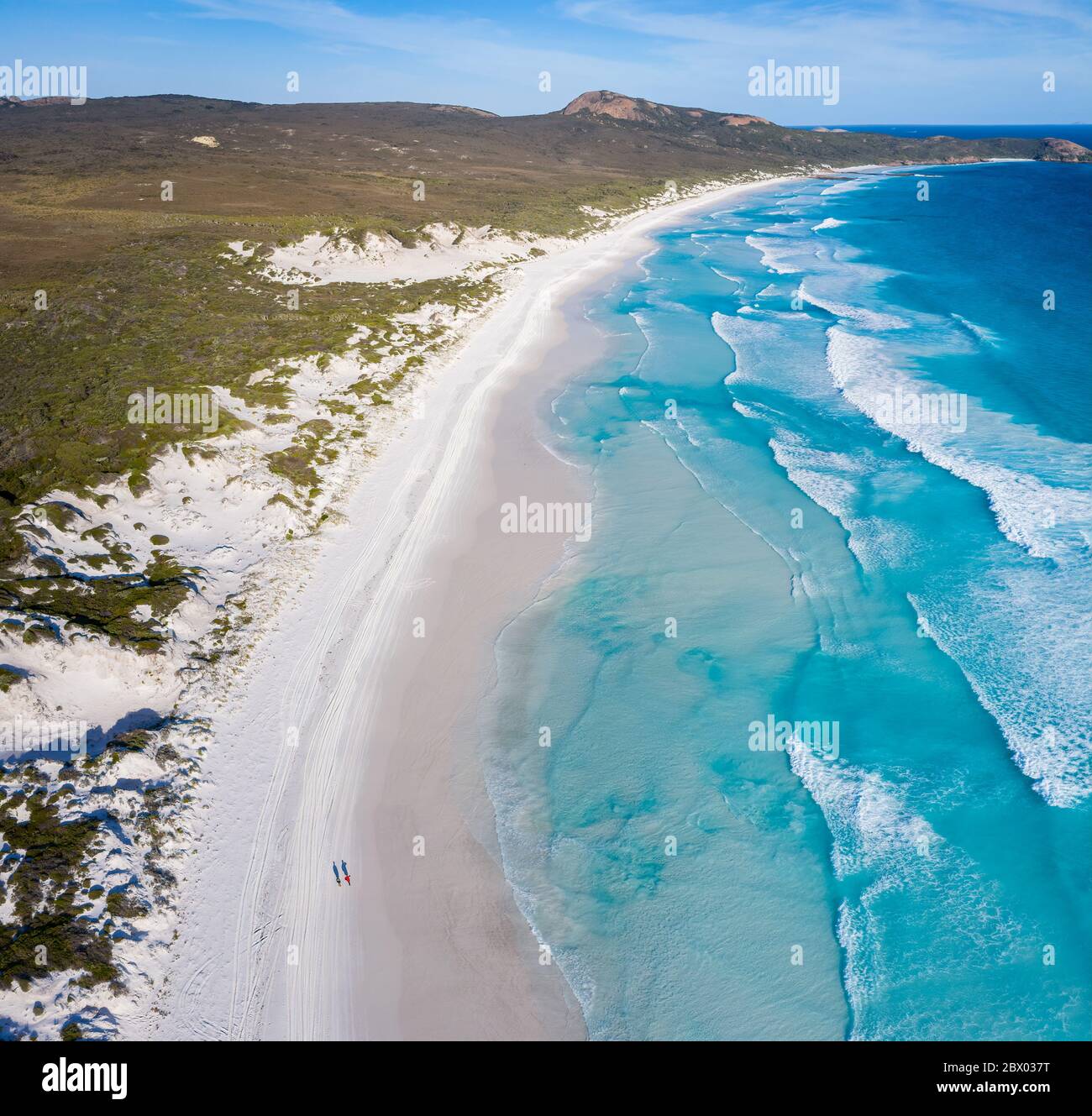 Drei Viertel der Sicht über dem Kopf auf zwei Personen, die am Lucky Bay Beach entlang am klaren, türkisfarbenen Wasser in Westaustralien spazieren Stockfoto