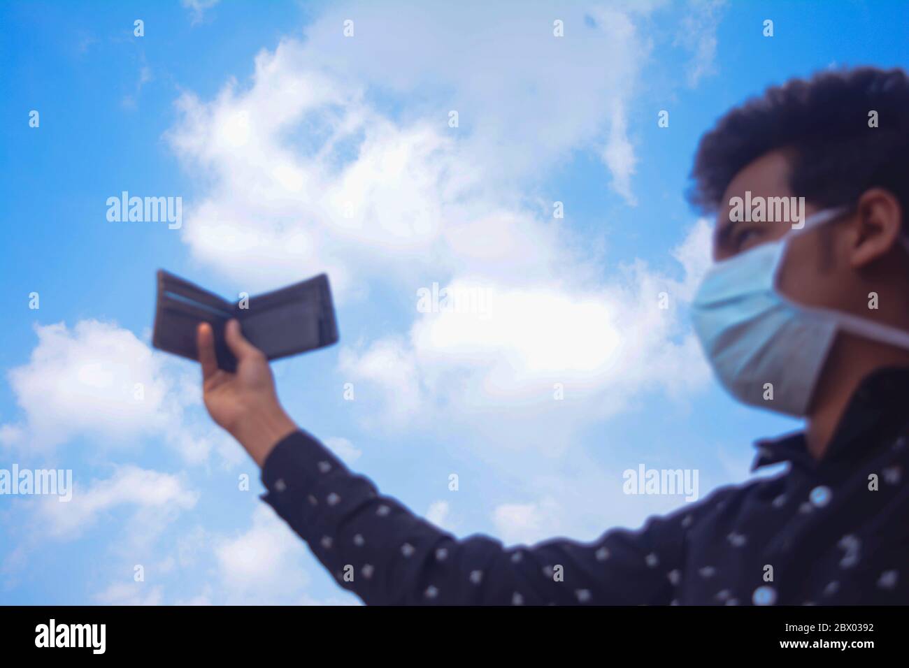 Mann mit Gesichtsmaske und zeigt seine Brieftasche auf blauen Himmel background.selective Fokus auf Himmel. Stockfoto