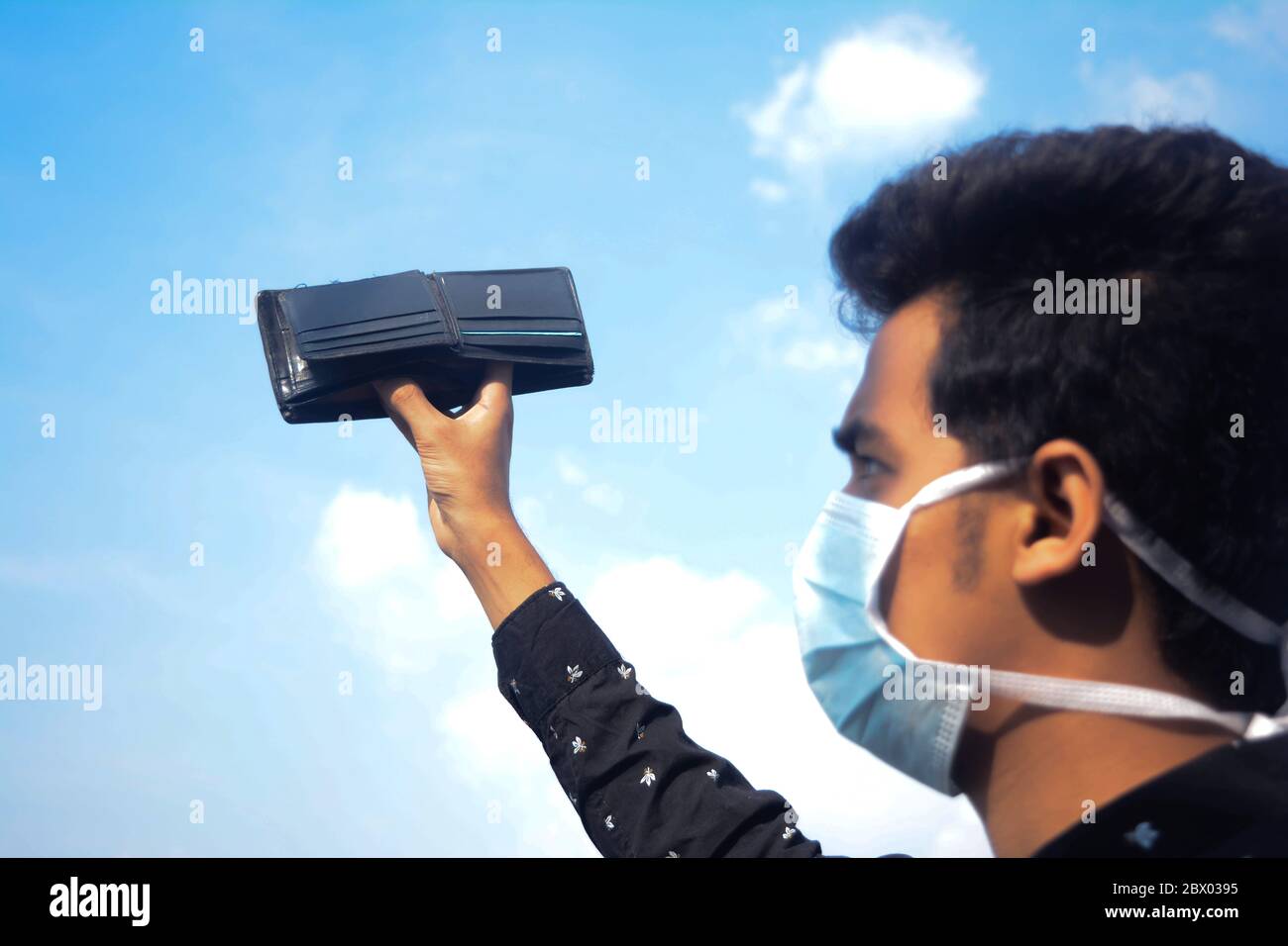 Junger Mann mit schützender Gesichtsmaske und zeigt seine leere Brieftasche auf Wolke und Himmel background.selective Fokus auf Brieftasche. Stockfoto